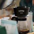 Person using a coffee brewing device with 'hoop' branding on a blurred background